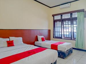 - une chambre avec 2 lits dotés de draps rouges et blancs dans l'établissement RedDoorz Syariah @ Hotel Sidomulyo Pacitan, à Pacitan
