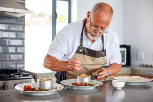 OnTheRocksBB Solar Powered Guesthouse and Ocean Lodge في بيتيس باي: رجل يعد الطعام في مطبخ مع أطباق من الطعام