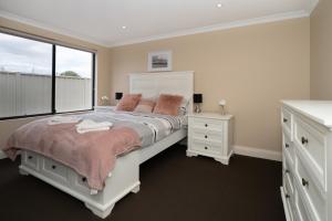 a bedroom with a white bed with pink pillows and a window at Ocean View Executive Apartment 2 in Busselton