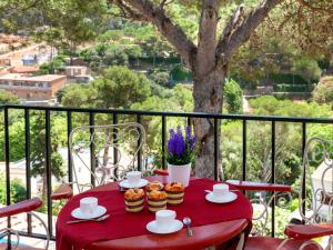 une table rouge avec des tasses et des muffins sur un balcon dans l'établissement Apartment S'Olivera-2 by Interhome, à Begur