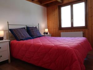 um quarto com uma cama com um edredão vermelho e 2 janelas em Apartment Cassiopée 26 by Interhome em Les Rasses