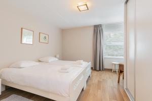 a white bedroom with two beds and a window at Hello Zeeland - Appartement Loverendale 10 in Domburg