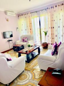 una sala de estar con sofás blancos y una mesa. en Crystal Apartments and Hotel, en Entebbe