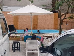 a woman sitting at a table under an umbrella near a swimming pool at Casa Bom Sossego in Boicucanga