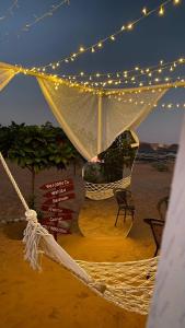 - un hamac avec des lumières et une chaise sur la plage dans l'établissement Wahiba Bedouin Rustic Camp, à Muntarib