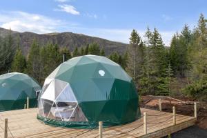 two green tents on a deck with mountains in the background at Golden Circle Domes - Glamping Experience in Selfoss