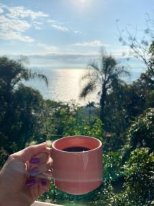 een persoon met een kopje koffie en uitzicht op de oceaan bij Double Deck - Linda vista com Jacuzzi in Palhoça
