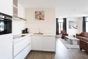 une cuisine avec des placards blancs et un salon dans l'établissement Hello Zeeland - Appartement Wijngaerde Residence 19, à Domburg