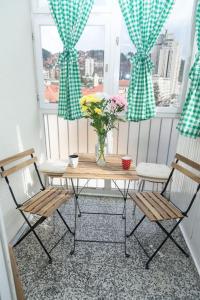een tafel met stoelen en een vaas met bloemen op een raam bij Apartman Panorama Glavna ulica in Užice