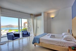 a bedroom with a bed and two chairs and a large window at Villa Marina by PosarelliVillas in Elounda +43 photos