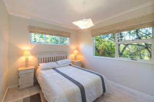 a bedroom with a bed with two night stands and two windows at Kostaplenti in Natureʼs Valley