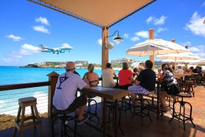 a group of people sitting at a bar with an airplane flying over the ocean at Maho Beach House - Spacious 1 Bedroom Suite in Maho Reef