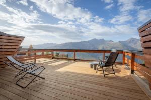 2 sedie e un tavolo su una terrazza di legno con montagne di La Cachette, Friendly Hotel & Spa ad Arc 1600
