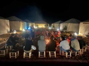 Un gruppo di persone sedute intorno al fuoco di notte di Ahlam Luxury Camp a Merzouga