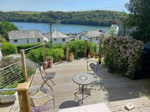 a wooden deck with chairs and tables and a view of the water at Truly Paradise Cottage in Golant