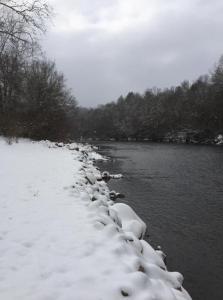 a snow covered path next to a body of water at Astounding River View in Copperhill