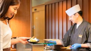 Eine Frau gibt einem Mann eine Schüssel Essen in der Unterkunft Kyukamura Minami-Izu in Minamiizu