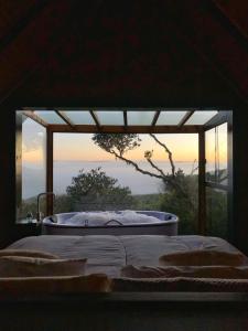 Bett in einem Zimmer mit einer Badewanne vor einem Fenster in der Unterkunft Morada Alto Das Nuvens in São José dos Ausentes