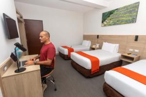 un hombre de pie en un escritorio en una habitación de hotel con dos camas en Casa Andina Standard Cusco San Blas, en Cusco