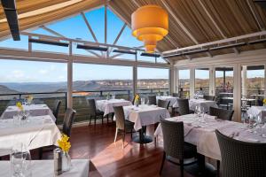 un restaurante con mesas y sillas blancas y ventanas en Echoes Boutique Hotel & Restaurant Blue Mountains, en Katoomba