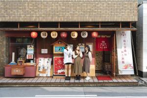 Tre donne sono in piedi davanti a un negozio di Cat Spa & Cat Ryokan by Neco Republic Osaka ad Osaka