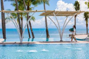 a woman walking by a swimming pool at a resort at Outrigger Koh Samui Beach Resort - SHA Extra Plus in Lamai