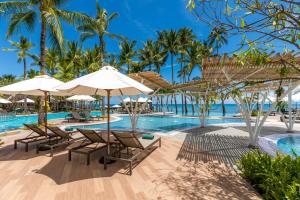 a resort pool with chairs and umbrellas and palm trees at Outrigger Koh Samui Beach Resort - SHA Extra Plus in Lamai