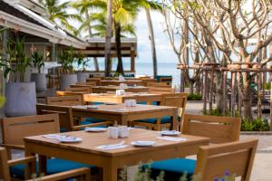 un restaurant avec des tables et des chaises en bois et l'océan dans l'établissement Outrigger Koh Samui Beach Resort - SHA Extra Plus, à Lamai