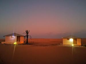 Deux petites maisons dans le désert la nuit dans l'établissement Safari Dunes Camp, à Ḩawīyah