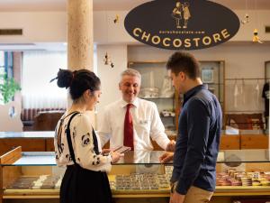 Un homme en chemise blanche et cravate parlant à deux personnes dans l'établissement Chocohotel, à Pérouse