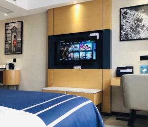 LanOu Hotel Yancheng Dafeng Yongtai Plaza في Dafeng: غرفة نوم بسرير وتلفزيون على جدار