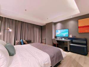a bedroom with a bed and a desk and a television at LanOu Hotel Bazhou Korla Jindu Plaza in Korla