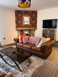 un sofá de cuero marrón en una sala de estar con chimenea en The Annex at Meadow Farm en Cambridge