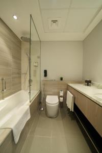 a bathroom with a tub and a toilet and a sink at DAMAC Hills 2 Hotel, an Edge by Rotana Hotel in Dubai