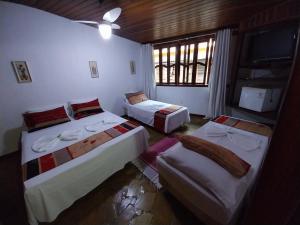 a bedroom with three beds and a tv and a window at Pousada toca do cambu in Angra dos Reis