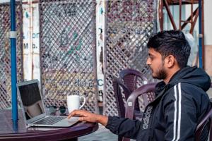 a man sitting at a table using a laptop computer at Triple One Hotel Tapovan Rishikesh,Near Laxman Jhula in Rishīkesh