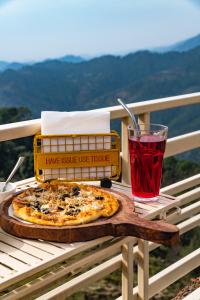 a pizza sitting on a table with a red drink at Jot Eco Boutique Stays in Dharamshala