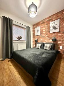 a bedroom with a black bed and a brick wall at LuxApart Kalisz Loft in Kalisz