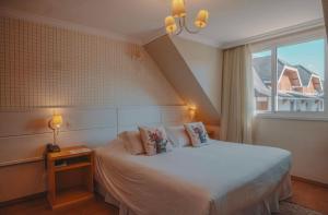 a bedroom with a white bed with a window at Pousada Telhado de Ouro in Campos do Jordão