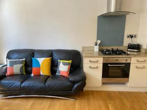 a black leather couch with colorful pillows in a kitchen at Sight Flats - SF01 - One Bedroom in London
