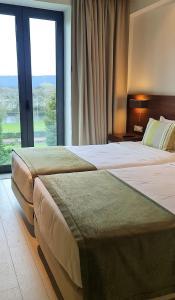 two beds in a hotel room with a large window at INATEL Cerveira Hotel in Vila Nova de Cerveira