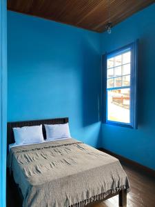 Dormitorio azul con cama y ventana en Casa estilo colonial, no Centro de Aiuruoca-MG., en Aiuruoca