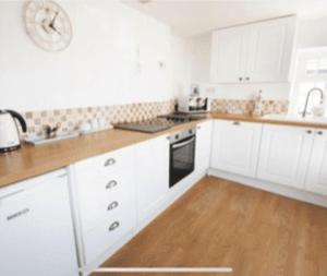 a kitchen with white cabinets and a wooden floor at Cosy Cottage Real Fire Nearby Pub Garden Parking in Altarnun