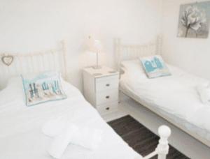 a white bedroom with two beds and a night stand at Cosy Cottage Real Fire Nearby Pub Garden Parking in Altarnun