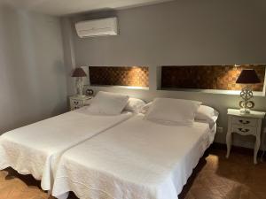 a bedroom with two beds with white sheets and lamps at Apartamento rural jama in Cilleros