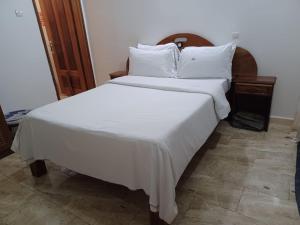 a large bed with white sheets and pillows at La Mboroise in Mboro