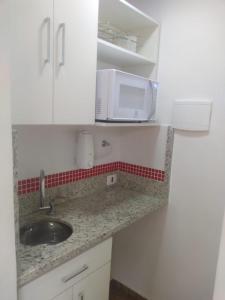 eine Küchentheke mit einer Spüle und einer Mikrowelle in der Unterkunft Flat na 16 de março, centro Historico de Petropolis in Petrópolis