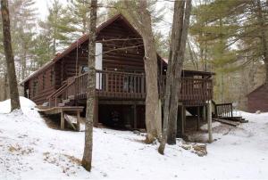 une cabane en rondins dans les bois dans la neige dans l'établissement Camp Voyager Log Cabin resort pool, golf, trails, lakes more, à Webb Lake