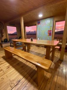 una mesa de madera y un banco en una habitación con ventanas en Vista al Paine - Refugio de Aventura, en Torres del Paine