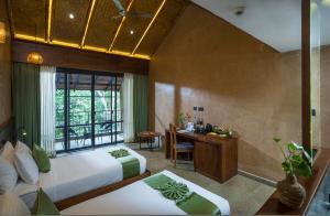 a bedroom with two beds and a desk and a window at Klov Resort & Spa in Wayanad